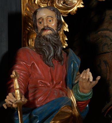 Zdjęcie nr 1: Rzeźba drążona, przedstawiająca św. Pawła. Święty ustawiony frontalnie w kontrapoście z lewą nogą ugiętą w kolanie, w prawej dłoni wyciągniętej przed siebie trzyma miecz zwrócony ostrzem w dół. Twarz pociągła o wyrazistych rysach, długim i prostym nosie, okolona długą brodą, oczy duże, włosy średniej długości, ciemnobrązowe. Święty ubrany jest w długą, czerwoną suknię, przewiązaną w pasie oraz złoty płaszcz z niebieską podszewką owinięty wokół lewego ramienia. Polichromia ciała naturalistyczna, płaszcz i atrybuty złocone.



