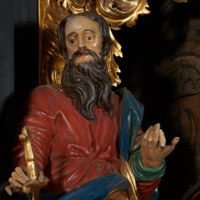 Zdjęcie nr 1: Rzeźba drążona, przedstawiająca św. Pawła. Święty ustawiony frontalnie w kontrapoście z lewą nogą ugiętą w kolanie, w prawej dłoni wyciągniętej przed siebie trzyma miecz zwrócony ostrzem w dół. Twarz pociągła o wyrazistych rysach, długim i prostym nosie, okolona długą brodą, oczy duże, włosy średniej długości, ciemnobrązowe. Święty ubrany jest w długą, czerwoną suknię, przewiązaną w pasie oraz złoty płaszcz z niebieską podszewką owinięty wokół lewego ramienia. Polichromia ciała naturalistyczna, płaszcz i atrybuty złocone.



