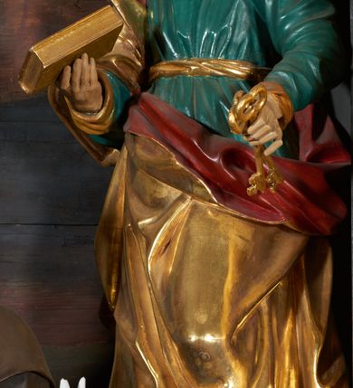 Zdjęcie nr 1: Rzeźba drążona, przedstawiająca św. Piotra. Święty ustawiony frontalnie w kontrapoście z lewą nogą ugiętą w kolanie, w lewej dłoni wyciągniętej przed siebie trzyma klucze, a w prawej zamkniętą księgę. Twarz pociągła o wyrazistych rysach, długim i prostym nosie, okolona krótką brodą, czoło wysokie z zakolami, oczy duże, nos wydatny, usta lekko rozchylone. Święty ubrany jest w długą, zieloną suknię, przewiązaną w pasie złotą szarfą oraz złoty płaszcz z czerwoną podszewką owinięty wokół prawego ramienia. Polichromia ciała naturalistyczna, płaszcz i atrybuty złocone.