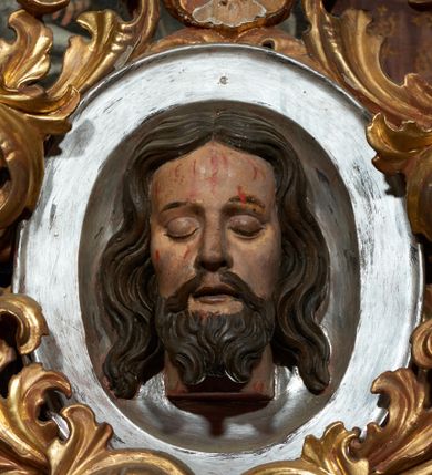 Zdjęcie nr 1: Na owalnej tacy, ukazana frontalnie płaskorzeźbiona głowa św. Jana Chrzciciela. Twarz szczupła o łagodnych rysach, zamkniętych oczach, długim nosie, okolona ciemną brodą. Włosy długie, ciemne w spływające po bokach w postaci fal, z przedziałkiem na środku głowy. Na twarzy i szyi ślady krwi. Wokół tacy obfity i plastycznie kształtowany, ażurowy suchy akant. Polichromia naturalistyczna, akant złocony.