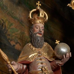 Zdjęcie nr 1: Rzeźba ścięta z tyłu, przedstawiająca św. Stefana. Święty ukazany frontalnie w postawie stojącej z jabłkiem królewskim w prawej dłoni i berłem w lewej. Twarz podłużna o dużych oczach, lekko rozchylonych ustach, okolona długą, bujną, czarną brodą. Święty ubrany jest w strój szlachecki, składający się z wysokich butów, srebrzonego kontusza przepasanego w partii bioder, zapinanego na guzy oraz przerzuconego przez ramiona, spiętego na piersi złotego płaszcza z czerwoną podszewką, ozdobionego kaboszonami i rautami na lamówce. Polichromia naturalistyczna w partiach ciała, szaty i atrybuty złocone i srebrzone.