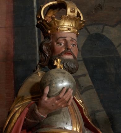 Zdjęcie nr 1: Rzeźba ścięta z tyłu, przedstawiająca św. Władysława. Święty ukazany frontalnie z jabłkiem królewskim w prawej dłoni i toporem w lewej. Twarz podłużna o głęboko osadzonych oczach i krótkim nosie, okolona brodą. Włosy półdługie, falowane. Święty ubrany jest w pełną, srebrną zbroję płytową, niebieską tunikę lamowaną złotem oraz złoty płaszcz spięty klamrą, podbity czerwienią, obficie drapowany w dolnej partii, w górnej zdobiony rautami i kaboszonami, na głowie ma założoną koronę zamkniętą. Polichromia naturalistyczna w partiach ciała, strój i atrybuty złocone i srebrzone.

