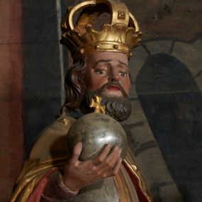 Zdjęcie nr 1: Rzeźba ścięta z tyłu, przedstawiająca św. Władysława. Święty ukazany frontalnie z jabłkiem królewskim w prawej dłoni i toporem w lewej. Twarz podłużna o głęboko osadzonych oczach i krótkim nosie, okolona brodą. Włosy półdługie, falowane. Święty ubrany jest w pełną, srebrną zbroję płytową, niebieską tunikę lamowaną złotem oraz złoty płaszcz spięty klamrą, podbity czerwienią, obficie drapowany w dolnej partii, w górnej zdobiony rautami i kaboszonami, na głowie ma założoną koronę zamkniętą. Polichromia naturalistyczna w partiach ciała, strój i atrybuty złocone i srebrzone.
