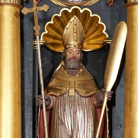 Zdjęcie nr 1: Rzeźba ścięta z tyłu, przedstawiająca św. Wojciecha. Święty ustawiony frontalnie, w lekkim kontrapoście z prawą nogą ugiętą w kolanie. W lewej ręce trzyma wiosło, a w prawej krzyż patriarchalny. Twarz o starczych rysach, na wpół przymkniętych oczach, rozchylonych ustach; okolona siwą brodą. Włosy siwe, średniej długości, zasłaniające uszy. Święty ubrany jest w fioletową albę, srebrną komżę, złotą kapę z czerwonym podbiciem, spiętą na piersi, złotą stułę, fioletowe rękawice, złotą infułę i brązowe buty. Kapa i infuła ozdobione są kaboszonami i rautami. Polichromia ciała naturalistyczna, szaty i atrybuty złocone i srebrzone.