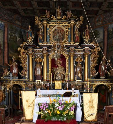 Zdjęcie nr 1: Nastawa ołtarzowa architektoniczna, trójosiowa, dwukondygnacyjna na cokole z bramkami. Ołtarz prostopadłościenny, drewniany. Mensa drewniana z kamiennym portatylem. Antepedium w formie leżącego prostokąta z przedstawieniem pelikana karmiącego młode. Całość ujęta bujną dekoracją roślinną z kwiatami ukazaną na złotym tle. U dołu napis: „A(NNO) D(OMINI) M C M X X I V”. Tabernakulum nowe w formie prostopadłościennej skrzynki. Na ściance frontowej drzwiczki w kształcie stojącego prostokąta zamkniętego łukiem nadwieszonym. W polu płaskorzeźbiony kielich z hostią oraz winna latorośl, powyżej dwa anioły. Nastawa ustawiona na zdwojonym cokole. Cokół dekorowany akantem mięsistym, owocowymi girlandami oraz uskrzydlonymi główkami anielskimi  na osi kolumn.

Osie pierwszej kondygnacji retabulum wydzielone czterema kolumnami o kapitelach korynckich ustawionymi na tle pilastrów, dźwigającymi pełne belkowanie zamknięte wydatnym gzymsem, wyłamane w partii podpór; nad polem środkowym przyjmujące formę łuku odcinkowego; na osi zewnętrznej pary podpór przerwany, odwrócony przyczółek. W polu środkowym rama w formie stojącego prostokąta zamkniętego łukiem półkolistym, w której umieszczona jest rzeźbiona Pieta. Na zasuwie obraz św. Jana Chrzciciela. Rama zdobiona ornamentem roślinnym, w przyłuczach uskrzydlone główki anielskie. Powyżej medalion z rzeźbioną głową św. Jana Chrzciciela na tacy w ramie z mięsistego, ażurowego akantu. W osiach bocznych płytkie nisze z figurami św. Wojciecha po lewej stronie i św. Stanisława po prawej. Nisze w osiach bocznych zamknięte konchą, ponad którą wstęga z koszem i owocami. Fryz dekorowany girlandami z tkaniny i owoców oraz uskrzydlonymi główkami anielskimi na osi podpór. Kondygnacja ujęta bujnymi uszami z ażurowego, suchego akantu. 

Druga kondygnacja szerokości osi środkowej, ujęta parą kolumn o kapitelach korynckich dźwigających pełne belkowanie z wydatnym gzymsem wyłamane na ich osi oraz przerwany przyczółek. W polu środkowym rama w formie stojącego prostokąta o ściętych narożach z obrazem Matki Boskiej. Kondygnacja flankowana przez figury św. Barbary po lewej stronie i św. Katarzyny po prawej. Z kolei na osi skrajnych kolumn, za przyczółkami ustawiona jest druga para dwóch świętych prawdopodobnie węgierskich. Fryz dekorowany akantem oraz uskrzydlonymi główkami anielskimi na osi podpór. Kondygnacja ujęta ażurowym suchym akantem. Na szczycie figura tronującej Matki Boskiej Królowej Niebios, stojącej na półksiężycu w glorii oraz dwa putta.
Bramki z przejściem w formie stojącego prostokąta zamkniętego łukiem półkolistym, ujęte pilastrami dźwigającymi niepełne belkowanie zamknięte silnie wystającym gzymsem i falistym, przerwanym przyczółkiem z siedzącymi puttami. Ponad bramkami na cokołach ustawione są figury św. Stefana po lewej stronie i św. Władysława po prawej. Drzwiczki bramek z malowanymi przedstawieniami św. Piotra po lewej stronie i św. Pawła po prawej. W przyłuczach i fryzie akant.
Nastawa marmoryzowana  w kolorze ciemnej zieleni ze złoconymi oraz srebrzonymi detalami architektonicznymi i ornamentyką. Na odwrociu ołtarza znajduje się malowidło przedstawiające św. Marię Magdalenę.
