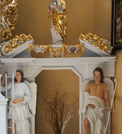 Zdjęcie nr 4: Rzeźba drążona, ustawiona na niewielkim postumencie. Figura zwrócona delikatnie w prawo, z prawą nogą ugiętą w kolanie, w lewej ręce trzyma gąbkę z octem na długim drzewcu. Twarz jest podłużna o pełnych policzkach oraz cofniętej brodzie; usta małe i delikatnie rozchylone, nos długi, oczy wąskie. Włosy są brązowe, falowane, sięgające do ramion. Anioł ubrany jest w długą, obficie marszczoną, białą szatę odsłaniającą nagi tors i prawą nogę. Polichromia naturalistyczna w partiach ciała, szaty i atrybuty białe.


