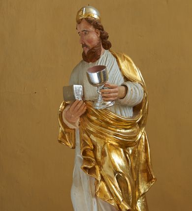 Zdjęcie nr 1: Rzeźba drążona, ustawiona na półkolistym postumencie, przedstawiająca Melchizedeka. Figura zwrócona jest trzy czwarte w prawo z naczyniem w prawej dłoni i kielichem w lewej. Twarz znacznie wydłużona, nieproporcjonalna, okolona jasnobrązowymi włosami i brodą. Włosy średniej długości, zawinięte w bujne loki. Melchizedek ubrany jest w długą, białą suknię, przewiązaną w talii oraz swobodnie zarzucony na plecy złocony płaszcz, odsłaniający prawe ramię, na głowie ma założone nakrycie kapłana żydowskiego. Polichromia naturalistyczna w partiach ciała, płaszcz złocony, atrybuty srebrzone.