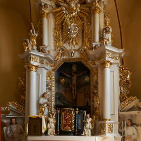Zdjęcie nr 1: Rzeźba przedstawia św. Weronikę. Figura ustawiona na niewielkim, prostopadłościennym cokole. Święta ukazana w pozycji stojącej, frontalnie z rękami uniesionymi, w których trzyma veraikon. Twarz podłużna o pełnych policzkach i podbródku, z małymi i delikatnie otwartymi ustami, krótkim nosem i wyraźnie zaznaczonymi łukami brwiowymi, policzki silnie zarumienione. Święta ubrana jest w długą, białą suknię ze złoconą chustą u szyi oraz złocony płaszcz założony na głowę; na stopach ma założone białe buty. Veraikon w formie srebrzonej chusty z płaskorzeźbioną twarzą Chrystusa skierowaną na wprost. Twarz okolona krótką, ciemnobrązową brodą; włosy ułożone w dwa skręcone pukle, spływające do przodu. Spod zielonej korony cierniowej spływają strużki krwi. Polichromia naturalistyczna w partiach ciała, płaszcz złocony, chusta srebrzona.