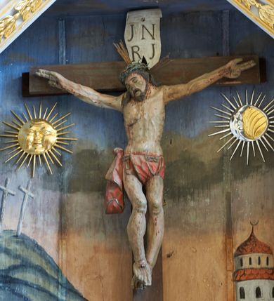 Zdjęcie nr 6: Nastawa ołtarzowa architektoniczna, jednoosiowa, dwukondygnacyjna, na cokole z bramkami. Ołtarz prostopadłościenny, drewniany; mensa drewniana. Antepedium w formie leżącego prostokąta, ujęte z trzech stron listwą o złoconym profilu, w centrum malowany złotem monogram maryjny. Tabernakulum w formie skrzynki o wklęsło-wypukłym wykroju, ustawione na profilowanym cokole, flankowane czterema kolumienkami o marmoryzowanych na niebiesko trzonach, podtrzymującymi niepełne belkowanie i wydatny gzyms. Ścianki boczne dekorowane prostokątnymi, marmoryzowanymi na niebiesko płycinami w złoconych ramach. Drzwiczki w kształcie stojącego prostokąta, zamkniętego łukiem nadwieszonym; w polu krucyfiks osadzony na wolutowej podstawie, od której odchodzą dwie gałązki akantu. Po bokach drzwiczek dwie wici roślinne. Tabernakulum flankują ustawione dwie figury aniołów.
Pierwsza kondygnacja retabulum ustawiona na cokole, ujęta parą filarów i stojących przed nimi, ustawionymi pod kątem kolumnami o kapitelach korynckich, dźwigających pełne belkowanie z wydatnym gzymsem. W polu środkowym rama w kształcie stojącego prostokąta zamkniętego trzema bokami z ośmioboku, dekorowana kampanulami, ujęta festonami z kampanulami, kwiatami i owocami. W polu obrazowym krucyfiks ukazany na malowanym tle Golgoty. Po bokach tabernakulum ustawione dwie figury: św. Jana Ewangelisty po lewej i św. Łukasza po prawej stronie.
Pośrodku belkowania zawieszone duże serce przebite sześcioma mieczami. Po jego bokach dwie rzeźby aniołków. Na gzymsie, na osi kolumny po prawej stronie ustawiona jest rzeźba św. Weroniki, a przed nią siedzący aniołek z trzema gwoździami w dłoni. Po lewej stronie św. Maria Magdalena, a przed nią aniołek z młotkiem w dłoni. 
Druga kondygnacja jest węższa, ujęta parą pilastrów i parą dostawionych pod kątem kolumn o kapitelach kompozytowych, dźwigających imposty. Cokoły kolumn i imposty ozdobione są z każdej strony uskrzydlonymi główkami aniołków. W polu rama w kształcie stojącego prostokąta o ściętych narożach, zdobiona ornamentem roślinnym, ujęta ornamentem z akantu i karbowanej wstęgi. Pośrodku promienista gloria z rzeźbioną gołębicą Ducha Świętego na tle obłoków. Całość zwieńczona drugą promienistą glorią z półpostacią Boga Ojca na tle obłoków. Po bokach na osi podpór siedzą dwie rzeźby aniołków. Obie kondygnacje ujęte są uszami utworzonymi z akantu i karbowanej wstęgi.
Bramki z przejściami w formie stojącego prostokąta o ściętych górnych narożach, zamknięte wydatnym gzymsem dźwiganym przez fragmenty pilastrów, na ich osi przerwany trójkątny przyczółek, zdobiony akantem. Przejścia flankowane figurami aniołów z arma Christi, nad bramkami figury proroków.
Struktura polichromowana na biało, ornamentyka i detale architektoniczne złocone i srebrzone.

