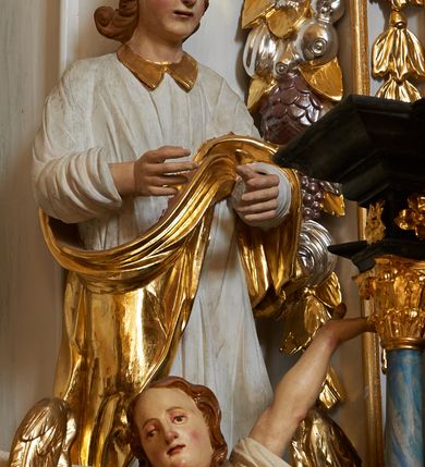 Zdjęcie nr 5: Nastawa ołtarzowa architektoniczna, jednoosiowa, dwukondygnacyjna, na cokole z bramkami. Ołtarz prostopadłościenny, drewniany; mensa drewniana. Antepedium w formie leżącego prostokąta, ujęte z trzech stron listwą o złoconym profilu, w centrum malowany złotem monogram maryjny. Tabernakulum w formie skrzynki o wklęsło-wypukłym wykroju, ustawione na profilowanym cokole, flankowane czterema kolumienkami o marmoryzowanych na niebiesko trzonach, podtrzymującymi niepełne belkowanie i wydatny gzyms. Ścianki boczne dekorowane prostokątnymi, marmoryzowanymi na niebiesko płycinami w złoconych ramach. Drzwiczki w kształcie stojącego prostokąta, zamkniętego łukiem nadwieszonym; w polu krucyfiks osadzony na wolutowej podstawie, od której odchodzą dwie gałązki akantu. Po bokach drzwiczek dwie wici roślinne. Tabernakulum flankują ustawione dwie figury aniołów.
Pierwsza kondygnacja retabulum ustawiona na cokole, ujęta parą filarów i stojących przed nimi, ustawionymi pod kątem kolumnami o kapitelach korynckich, dźwigających pełne belkowanie z wydatnym gzymsem. W polu środkowym rama w kształcie stojącego prostokąta zamkniętego trzema bokami z ośmioboku, dekorowana kampanulami, ujęta festonami z kampanulami, kwiatami i owocami. W polu obrazowym krucyfiks ukazany na malowanym tle Golgoty. Po bokach tabernakulum ustawione dwie figury: św. Jana Ewangelisty po lewej i św. Łukasza po prawej stronie.
Pośrodku belkowania zawieszone duże serce przebite sześcioma mieczami. Po jego bokach dwie rzeźby aniołków. Na gzymsie, na osi kolumny po prawej stronie ustawiona jest rzeźba św. Weroniki, a przed nią siedzący aniołek z trzema gwoździami w dłoni. Po lewej stronie św. Maria Magdalena, a przed nią aniołek z młotkiem w dłoni. 
Druga kondygnacja jest węższa, ujęta parą pilastrów i parą dostawionych pod kątem kolumn o kapitelach kompozytowych, dźwigających imposty. Cokoły kolumn i imposty ozdobione są z każdej strony uskrzydlonymi główkami aniołków. W polu rama w kształcie stojącego prostokąta o ściętych narożach, zdobiona ornamentem roślinnym, ujęta ornamentem z akantu i karbowanej wstęgi. Pośrodku promienista gloria z rzeźbioną gołębicą Ducha Świętego na tle obłoków. Całość zwieńczona drugą promienistą glorią z półpostacią Boga Ojca na tle obłoków. Po bokach na osi podpór siedzą dwie rzeźby aniołków. Obie kondygnacje ujęte są uszami utworzonymi z akantu i karbowanej wstęgi.
Bramki z przejściami w formie stojącego prostokąta o ściętych górnych narożach, zamknięte wydatnym gzymsem dźwiganym przez fragmenty pilastrów, na ich osi przerwany trójkątny przyczółek, zdobiony akantem. Przejścia flankowane figurami aniołów z arma Christi, nad bramkami figury proroków.
Struktura polichromowana na biało, ornamentyka i detale architektoniczne złocone i srebrzone.

