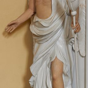 Zdjęcie nr 1: Rzeźba ścięta z tyłu, ustawiona na postumencie. Figura ukazana frontalnie, w kontrapoście z lewą nogą ugiętą w kolanie, w lewej ręce trzyma pochodnię, prawą wyciąga w bok, skrzydła złożone. Twarz owalna, o pełnych policzkach, bez indywidualnych rysów fizjonomii z delikatnie rozchylonymi ustami. Włosy ciemnobrązowe, w postaci loków opadają na plecy. Anioł ubrany jest w białą szatę odsłaniającą tors, prawe ramię i lewą nogę. Szata jest gęsto drapowana. Polichromia w odsłoniętych partiach ciała naturalistyczna.