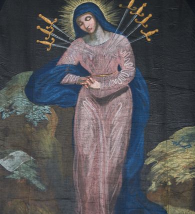 Zdjęcie nr 3: Tkanina w kształcie stojącego prostokąta, zamkniętego łukiem nadwieszonym, dosztukowana do kształtu stojącego prostokąta. W centrum kompozycji stojąca Matka Boska, ukazana frontalnie z dłońmi splecionymi na wysokości bioder z głową przechyloną w prawo i skłonioną delikatnie w dół, prawą ręką opiera się o skałę. W jej serce wbite jest siedem mieczy: trzy z lewej strony i cztery z prawej. Twarz trójkątna o wyraźnych, konturowych rysach, oczy zamknięte, duży nos. Ubrana jest w różową suknię i granatowy płaszcz przerzucony przez prawą rękę i spływający wzdłuż lewego boku; na głowie ma granatowy welon, a wokół głowy złoty i promienisty nimb. Maria ukazana jest na tle skał: na skale po lewej stronie leży biały titulus w formie banderoli z napisem „IN / RI”, a na skale po prawej trzy gwoździe i korona cierniowa. Tło jednolite, czarne. Kolorystyka przytłumiona, wyraźnie podkreślona i rozświetlona jasnymi plamami barwnymi na sukni i twarzy Matki Boskiej. 