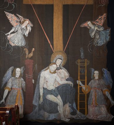 Zdjęcie nr 1: Tkanina wielkopostna przedstawiająca Piętę ukazaną na zszytych fragmentach płótna (25 brytów). W centrum kompozycji stoi krzyż, pod którym siedzi Matka Boska trzymająca na kolanach martwe ciało Chrystusa. Maria zwrócona jest trzy czwarte w lewo,  lewą ręką podtrzymuje rękę syna, prawą obejmuje go w talii, głowę ma przechyloną w lewo. Twarz podłużna o wyraźnych, konturowych rysach, oczy niemal zamknięte, długi nos, wąskie usta. Ubrana jest w jasną suknię o fałdach podkreślonych wyraźnymi konturami, niebieski płaszcz, okrywający nogi, podwikę oraz szary welon na głowie. Wokół głowy ma kolisty, złoty i promienisty nimb. Ciało Chrystusa spoczywa na kolanach Marii. Twarz owalna o konturowych rysach z zamkniętymi oczami, okolona jasnym zarostem, włosy długie z przedziałkiem na środku głowy, opadające na plecy. Ciało blade, ociekające krwią, niemodelowane, podkreślone konturem. Przez biodra przewiązane granatowe perizonium. O ramiona krzyża oparte ukośnie: po lewej włócznia, po prawej gąbka z octem na długim drzewcu. U góry krzyża zawieszony biały titulus w formie banderoli z tytułem winy w trzech językach „INRI”. Po bokach kompozycji u dołu, dwa anioły ukazane w pozycji klęczącej, zwrócone trzy czwarte ku środkowi obrazu. Anioł po prawej stronie trzyma w prawej dłoni drabinę, na której koniec założona jest korona cierniowa, nieco niżej ukazano trzy gwoździe, a wyżej rękawicę żołnierza. Anioł po lewej obejmuje kolumnę biczowania, na której stoi piejący kogut. W górnej części kolumny przywiązane są bicze. Ponad aniołami unoszą się na obłokach dwie kolejne postacie aniołów. Anioły ubrane są w różowe suknie i niebieskie tuniki z żółtą podszewką, przewiązane w pasie złotą taśmą. W górnych narożach obrazu symbole lunarne o ludzkich twarzach: po lewej księżyc, po prawej słońce. Na dole obrazu, pośrodku malowana na czerwono sygnatura „AB”. Po lewej stronie obrazu na wysokości ręki anioła unoszącego się na obłoku fragment daty „16”. Po bokach krzyża kilkuwersowe napisy, słabo czytelne. Według literatury nad głową Matki Boskiej znajduje się napis: „Filia populi ei acingere cilicio recospergere cinere: iuctu Unigenliafe tibi planctu emaru”.  Obok słońca i księżyca kolejny napis: „Ecce videntes clamabunt foris angeli pacis amare flebunt”, a także „amare flebunt angeli pacis”. Kolorystyka blada, w odcieniach zimnych, formy wydobyte konturem.