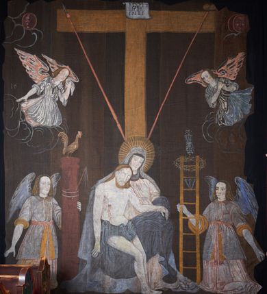 Zdjęcie nr 2: Tkanina wielkopostna przedstawiająca Piętę ukazaną na zszytych fragmentach płótna (25 brytów). W centrum kompozycji stoi krzyż, pod którym siedzi Matka Boska trzymająca na kolanach martwe ciało Chrystusa. Maria zwrócona jest trzy czwarte w lewo,  lewą ręką podtrzymuje rękę syna, prawą obejmuje go w talii, głowę ma przechyloną w lewo. Twarz podłużna o wyraźnych, konturowych rysach, oczy niemal zamknięte, długi nos, wąskie usta. Ubrana jest w jasną suknię o fałdach podkreślonych wyraźnymi konturami, niebieski płaszcz, okrywający nogi, podwikę oraz szary welon na głowie. Wokół głowy ma kolisty, złoty i promienisty nimb. Ciało Chrystusa spoczywa na kolanach Marii. Twarz owalna o konturowych rysach z zamkniętymi oczami, okolona jasnym zarostem, włosy długie z przedziałkiem na środku głowy, opadające na plecy. Ciało blade, ociekające krwią, niemodelowane, podkreślone konturem. Przez biodra przewiązane granatowe perizonium. O ramiona krzyża oparte ukośnie: po lewej włócznia, po prawej gąbka z octem na długim drzewcu. U góry krzyża zawieszony biały titulus w formie banderoli z tytułem winy w trzech językach „INRI”. Po bokach kompozycji u dołu, dwa anioły ukazane w pozycji klęczącej, zwrócone trzy czwarte ku środkowi obrazu. Anioł po prawej stronie trzyma w prawej dłoni drabinę, na której koniec założona jest korona cierniowa, nieco niżej ukazano trzy gwoździe, a wyżej rękawicę żołnierza. Anioł po lewej obejmuje kolumnę biczowania, na której stoi piejący kogut. W górnej części kolumny przywiązane są bicze. Ponad aniołami unoszą się na obłokach dwie kolejne postacie aniołów. Anioły ubrane są w różowe suknie i niebieskie tuniki z żółtą podszewką, przewiązane w pasie złotą taśmą. W górnych narożach obrazu symbole lunarne o ludzkich twarzach: po lewej księżyc, po prawej słońce. Na dole obrazu, pośrodku malowana na czerwono sygnatura „AB”. Po lewej stronie obrazu na wysokości ręki anioła unoszącego się na obłoku fragment daty „16”. Po bokach krzyża kilkuwersowe napisy, słabo czytelne. Według literatury nad głową Matki Boskiej znajduje się napis: „Filia populi ei acingere cilicio recospergere cinere: iuctu Unigenliafe tibi planctu emaru”.  Obok słońca i księżyca kolejny napis: „Ecce videntes clamabunt foris angeli pacis amare flebunt”, a także „amare flebunt angeli pacis”. Kolorystyka blada, w odcieniach zimnych, formy wydobyte konturem.