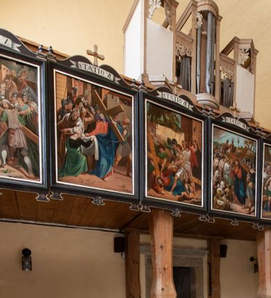 Zdjęcie nr 1: Parapet chóru oparty na dwóch profilowanych, drewnianych filarach. Na balustradzie stacje drogi krzyżowej. Prospekt organowy na wysokim, prostopadłościennym cokole; pięcioosiowy o zróżnicowanej wysokości osi: środkowa najwyższa o zarysie wypukłym, skrajne nieco niższe, trójkątnie występujące ku przodowi, druga i czwarta najniższe, płaskie. Całość zamknięta profilowanymi gzymsami. W górnej części prześwitów mieszczących piszczałki ornament akantowy.


