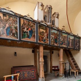 Zdjęcie nr 1: Parapet chóru oparty na dwóch profilowanych, drewnianych filarach. Na balustradzie stacje drogi krzyżowej. Prospekt organowy na wysokim, prostopadłościennym cokole; pięcioosiowy o zróżnicowanej wysokości osi: środkowa najwyższa o zarysie wypukłym, skrajne nieco niższe, trójkątnie występujące ku przodowi, druga i czwarta najniższe, płaskie. Całość zamknięta profilowanymi gzymsami. W górnej części prześwitów mieszczących piszczałki ornament akantowy.


