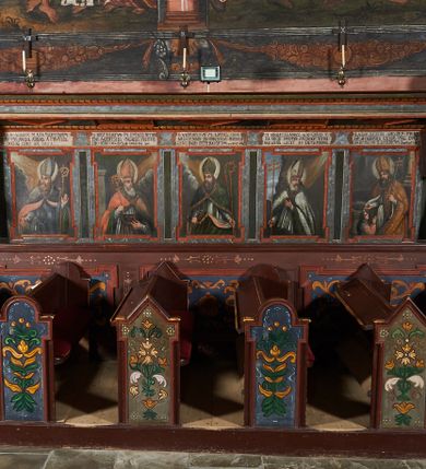 Zdjęcie nr 1: Para drewnianych stalli pięciosiedzeniowych z baldachimem. Przedpiersie w formie pulpitowej dekorowane od frontu płycinami z uszakami z malowaną na złoto dekorację kwiatową na niebieskim tle. Zaplecek dekorowany pięcioma obrazami biskupów i opatów węgierskich. Ścianki zaplecka wycięte wolutowo. Obrazy w kształcie stojących prostokątów z uszakami, oddzielone od siebie wąskimi płycinami w formie stojących prostokątów. Postacie przedstawione w popiersiu; zwrócone w trzech czwartych na tle obłoków i symbolicznie zaznaczonej architektury. Ponad obrazami łacińskie inskrypcje. Na stalli umieszczonej na ścianie północnej przedstawieni i opisani są kolejno od lewej:
1. Święty Bonifacy w stroju biskupim na tle chmur z pastorałem i mieczem w ręku: „S(ANCTUS) BONIFACIVS M. ADS. MARTINVM/IN VNGARCHI. ABBAS. A PRVFSIS./OCCISG. CIRC. AN(NO) 1007”;
2. Święty Bezertus trzyma w dłoni pastorał, miecz i księgę z kamieniami: „S(ANCTUS) BEZTERTVS M. EPISCO. NITRI/ENS. A.GENTHIB VNGARIS PESTHI./ PRO FIDE OCCISVS A 1047. 24 Sept.”;
3. Święty Gerard w stroju biskupim z pastorałem i dzidą w dłoni oraz z księgą z kamieniami: „S(ANCTUS) GEREARDVS M. EPISC. CHA/NADIENSIS IN VNGARIA BUDAE A./ GENTIB, INTFREMPTv. AB. 1047. 24”;
4. Błogosławiony Sebastian w stroju biskupim: „B(EATUS) SEBASTIANVS EX. ORD. S(ANCTUS) / BENED(ICTUS) PRIMVS ARCHIEP[ISCOPUS] STRI/ GONIENS OBIIT 30 DECEMBRIS.”;
5. Święty Wojciech w stroju biskupim chrzci klęczącego przed nim obok młodzieńca: „S(ANCTUS) ADALBERTVS ARCHIEP(ISCOPUS) PRAGEN/SIS A  DEIPARA GEYSAE VNG.  DVCI/SVBMISSUS S(ANCTUM) EMERICUM Baptisat Obiit An(no) 23”.

Na stalli południowej, od lewej:
1. Święty Pilgrim w stroju biskupi chrzci trójkę dzieci: „S(ANCTUS) PHILIGRINVS EP. LAVREACE/NS A GEYZA  VNGARORORVM DUCE/ IN VNGARIAM Vocatus Hunc… 5000 Vnogarorum Bautiso”
2. Święty Buldus w stroju biskupim trzyma w dłoni palmę męczeństwa i pastorał, a w drugiej dłoni księgę, na której leżą kamienie: „S(ANCTUS) BVLDVS M. EPISCO. AGRIENS. PRO FIDE LAPIDIRVS RT/ GLADIIS OCCVBVIT BUDAE ANNO 1046. 24”
3. Święty Gaudenty w albie, pelerynce i birecie z pastorałem w dłoni czyta księgę: „S(ANCTUS) GAVDENTIVS EP. S. ADALBERTI FRAT. ET IN VNG./CO APOST. CHRISTI Fidem Pramulgav[it]”
4. Święty Augustyn w stroju biskupim z pastorałem w dłoni „AVGVSTINVS EP. ZA/GRABIENSIS EX VNG. ORI/VNG? OBIIT 1332 3 Augusti”
5.  Błogosławiony Jan  w stroju biskupim z pastorałem w dłoni: „B(EATUS) IONANNES ORD[O] PRAEDIC[ATORUM]/ PER VNGARIAM PROVINCIALIS EP. BOSNENSIS OBIIT 1253. 4 Nov.”

Baldachim pulpitowy zwieńczony profilowanym gzymsem. W podniebieniu naprzemiennie płyciny romboidalne i prostokątne mieszczące malowaną dekorację w formie girland i rozet. Struktura malowana na kolor ciemnobrązowy, zaplecki marmoryzowane. Detal architektoniczny czerwony i niebieski.