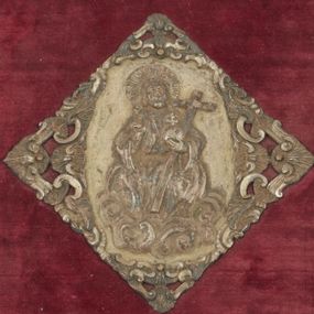 Zdjęcie nr 1: Okucia w kształcie częściowo ażurowych plakiet rozmieszczone na oprawie mszału wydanego w Wenecji w 1768 roku, na tle desek obciągniętych ciemnoczerwonym aksamitem. W narożach górnej i dolnej okładki trójkątne plakiety z motywami uskrzydlonych główek aniołów i ornamentem małżowinowym; przy krawędziach gładkie listwy łączące plakiety. Przy prawej krawędzi górnej okładziny i przy lewej krawędzi okładziny dolnej szyldziki zapięcia w formie bukietów kwiatów wyrastających z masek. Pośrodku okładzin rombowe plakiety z przedstawieniami – na górnej okładzinie Chrystus Salwator siedzący na obłokach, na dolnej Arma Christi; w narożach grzebienie ornamentu rocaille’owego (?) oraz motywy muszli i wolut. 