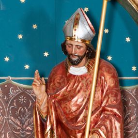 Zdjęcie nr 1: Rzeźba pełnoplastyczna przedstawiająca św. Stanisława Biskupa. Święty zwrócony jest delikatnie w prawo, pochylony delikatnie w dół w kierunku półpostaci Piotrowina. Prawą rękę wznosi ku górze w geście błogosławieństwa, w lewej opuszczonej w dół trzyma pastorał. Twarz trójkątna okolona ciemnym zarostem i długimi włosami spływającymi na plecy. Święty ubrany jest w białą albę z czerwonym pasem u dołu, wzorzysty ornat zdobiony szeroką bordiurą oraz czerwony ornat na planie koła dekorowany wicią roślinną; na głowie ma założoną srebrną infułę. U stóp biskupa, po lewej stronie ukazane jest popiersie Piotrowina przedstawione z prawego profilu, w białej szacie, z rękoma złożonymi w geście modlitewnym. Twarz szeroka z silnie wysuniętym podbródkiem z jasnym włosami schowanymi pod szatą, założoną na głowę. Polichromia w odsłoniętych partiach ciała naturalistyczna, detale złocone i srebrzone.