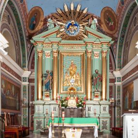 Zdjęcie nr 1: Nastawa architektoniczna, trójosiowa, jednokondygnacyjna ze zwieńczeniem, na podwójnym cokole zakończonym gzymsem. Ołtarz i mensa w marmurowej okładzinie, ustawione na czterostopniowym podwyższeniu na planie prostokąta o ściętych narożach. Tabernakulum w kształcie prostopadłościennej skrzynki, ujęte czterema kolumnami w narożach. Drzwiczki dwuskrzydłowe z aplikowanymi kielichem z hostią w glorii w otoczeniu kłosów zbóż i winnego grona. Tron wystawienia w formie półkolistej glorietty oraz półkopuły, zwieńczonej kulą z krzyżem.Osie wydzielone są dwiema parami kolumn korynckich, dźwigających pełne belkowanie wyłamane w ich partii oraz przerwany przyczółek z klęczącą parą aniołów. W polu osi bocznych pilastry; na ich tle wsporniki z figurami św. Piotra po lewej i św. Pawła po prawej. W polu środkowym rama w formie stojącego prostokąta, we wnęce płaskorzeźbione przedstawienie Matki Boskiej Różańcowej. Zwieńczenie w kształcie promienistej glorii o naprzemiennych falistych i prostych wiązkach promieni z rzeźbioną półpostacią Boga Ojca pośród obłoków. Cokoły dekorowane płycinami w formie stojącego prostokąta z uszakami. Rama obrazu profilowana, zdobiona kimationem; na wewnętrznych ściankach wnęki bujny akant. U spodu obrazu dwie wiązki akantu. Wsporniki dla figur utworzone są z palmet akantu oraz tralek. Architraw dekorowany jajownikiem oraz pasem perełkowania; fryz zdobiony stylizowanym akantem, nad polem środkowym ornament roślinny, na osiach kolumn rozety. Gzyms belkowania i przyczółka dekorowany kimationem, kostkowaniem i perełkowaniem.
Nastawa polichromowana na kolor jasnozielony z ciemnozielonymi detalami; kolumny, ornamentyka oraz detale architektoniczne złocone.