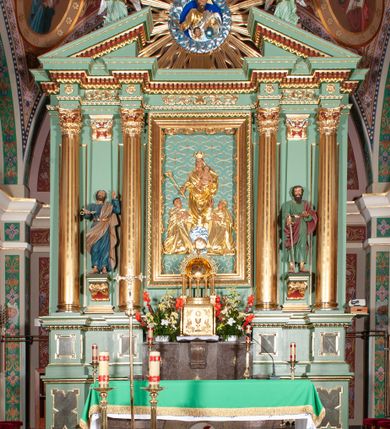 Zdjęcie nr 2: Nastawa architektoniczna, trójosiowa, jednokondygnacyjna ze zwieńczeniem, na podwójnym cokole zakończonym gzymsem. Ołtarz i mensa w marmurowej okładzinie, ustawione na czterostopniowym podwyższeniu na planie prostokąta o ściętych narożach. Tabernakulum w kształcie prostopadłościennej skrzynki, ujęte czterema kolumnami w narożach. Drzwiczki dwuskrzydłowe z aplikowanymi kielichem z hostią w glorii w otoczeniu kłosów zbóż i winnego grona. Tron wystawienia w formie półkolistej glorietty oraz półkopuły, zwieńczonej kulą z krzyżem.Osie wydzielone są dwiema parami kolumn korynckich, dźwigających pełne belkowanie wyłamane w ich partii oraz przerwany przyczółek z klęczącą parą aniołów. W polu osi bocznych pilastry; na ich tle wsporniki z figurami św. Piotra po lewej i św. Pawła po prawej. W polu środkowym rama w formie stojącego prostokąta, we wnęce płaskorzeźbione przedstawienie Matki Boskiej Różańcowej. Zwieńczenie w kształcie promienistej glorii o naprzemiennych falistych i prostych wiązkach promieni z rzeźbioną półpostacią Boga Ojca pośród obłoków. Cokoły dekorowane płycinami w formie stojącego prostokąta z uszakami. Rama obrazu profilowana, zdobiona kimationem; na wewnętrznych ściankach wnęki bujny akant. U spodu obrazu dwie wiązki akantu. Wsporniki dla figur utworzone są z palmet akantu oraz tralek. Architraw dekorowany jajownikiem oraz pasem perełkowania; fryz zdobiony stylizowanym akantem, nad polem środkowym ornament roślinny, na osiach kolumn rozety. Gzyms belkowania i przyczółka dekorowany kimationem, kostkowaniem i perełkowaniem.
Nastawa polichromowana na kolor jasnozielony z ciemnozielonymi detalami; kolumny, ornamentyka oraz detale architektoniczne złocone.