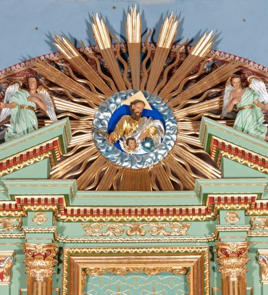 Zdjęcie nr 5: Nastawa architektoniczna, trójosiowa, jednokondygnacyjna ze zwieńczeniem, na podwójnym cokole zakończonym gzymsem. Ołtarz i mensa w marmurowej okładzinie, ustawione na czterostopniowym podwyższeniu na planie prostokąta o ściętych narożach. Tabernakulum w kształcie prostopadłościennej skrzynki, ujęte czterema kolumnami w narożach. Drzwiczki dwuskrzydłowe z aplikowanymi kielichem z hostią w glorii w otoczeniu kłosów zbóż i winnego grona. Tron wystawienia w formie półkolistej glorietty oraz półkopuły, zwieńczonej kulą z krzyżem.Osie wydzielone są dwiema parami kolumn korynckich, dźwigających pełne belkowanie wyłamane w ich partii oraz przerwany przyczółek z klęczącą parą aniołów. W polu osi bocznych pilastry; na ich tle wsporniki z figurami św. Piotra po lewej i św. Pawła po prawej. W polu środkowym rama w formie stojącego prostokąta, we wnęce płaskorzeźbione przedstawienie Matki Boskiej Różańcowej. Zwieńczenie w kształcie promienistej glorii o naprzemiennych falistych i prostych wiązkach promieni z rzeźbioną półpostacią Boga Ojca pośród obłoków. Cokoły dekorowane płycinami w formie stojącego prostokąta z uszakami. Rama obrazu profilowana, zdobiona kimationem; na wewnętrznych ściankach wnęki bujny akant. U spodu obrazu dwie wiązki akantu. Wsporniki dla figur utworzone są z palmet akantu oraz tralek. Architraw dekorowany jajownikiem oraz pasem perełkowania; fryz zdobiony stylizowanym akantem, nad polem środkowym ornament roślinny, na osiach kolumn rozety. Gzyms belkowania i przyczółka dekorowany kimationem, kostkowaniem i perełkowaniem.
Nastawa polichromowana na kolor jasnozielony z ciemnozielonymi detalami; kolumny, ornamentyka oraz detale architektoniczne złocone.