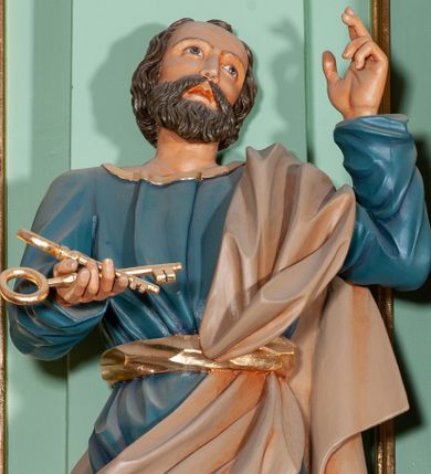 Zdjęcie nr 1: Rzeźba pełna, przedstawiająca św. Piotra. Święty ustawiony frontalnie z głową skierowaną w górę, przechyloną delikatnie w lewą stronę. W prawej, wyciągniętej przed siebie dłoni trzyma dwa złote klucze, a lewą unosi w geście oratorskim. Twarz szeroka, o delikatnie rzeźbionych rysach, oczach skierowanych ku górze; okolona krótką brodą. Włosy średniej długości, brązowe, delikatnie falowane, zasłaniające uszy. Ubrany jest w niebieską suknię, sięgającą do kostek ze złotą lamówką u szyi, przewiązaną w talii szerokim, złotym pasem. Przez lewe ramię i biodro przerzucony jest diagonalnie beżowy płaszcz. Spod tuniki widoczne są na stopach złote sandały.
Polichromia w odsłoniętych partiach ciała naturalistyczna, detale złocone.