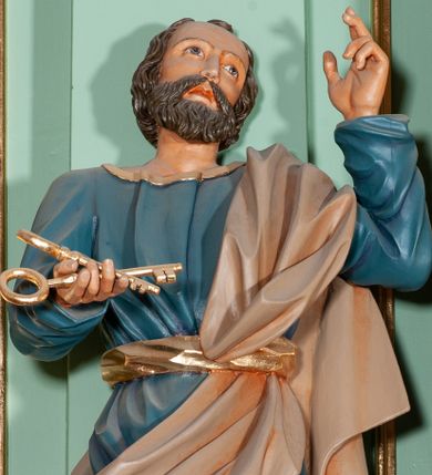 Zdjęcie nr 1: Rzeźba pełna, przedstawiająca św. Piotra. Święty ustawiony frontalnie z głową skierowaną w górę, przechyloną delikatnie w lewą stronę. W prawej, wyciągniętej przed siebie dłoni trzyma dwa złote klucze, a lewą unosi w geście oratorskim. Twarz szeroka, o delikatnie rzeźbionych rysach, oczach skierowanych ku górze; okolona krótką brodą. Włosy średniej długości, brązowe, delikatnie falowane, zasłaniające uszy. Ubrany jest w niebieską suknię, sięgającą do kostek ze złotą lamówką u szyi, przewiązaną w talii szerokim, złotym pasem. Przez lewe ramię i biodro przerzucony jest diagonalnie beżowy płaszcz. Spod tuniki widoczne są na stopach złote sandały.
Polichromia w odsłoniętych partiach ciała naturalistyczna, detale złocone.