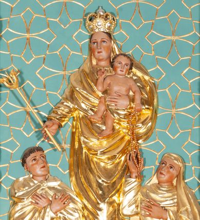 Zdjęcie nr 1: Kompozycja w kształcie stojącego prostokąta, w centrum płaskorzeźba z przedstawieniem Matki Boskiej stojącej na obłoku, na którym leżą jabłko królewskie i berło. Maria na lewym ręku trzyma Dzieciątko, a w prawej wyciągniętej przed siebie dzierży berło. Ubrana jest w suknię oraz w ściśle okalający jej ciało płaszcz; na głowie ma koronę zamkniętą. Twarz o delikatnych rysach, owalna. Dzieciątko ukazane jest w skręcie sylwetki, torsem zwrócone frontalnie; prawą rączka błogosławi, lewą podtrzymuje różaniec. U dołu klęczący św. Dominik oraz św. Katarzyna Sieneńska.  Po lewej św. Dominik zwrócony trzy czwarte w lewo, z głową skierowaną w górę oraz dłońmi skrzyżowanymi na piersi. Ubrany jest w habit i płaszcz dominikański , na głowie ma tonsurę. Po prawej stronie św. Katarzyna Sieneńska o analogicznym układzie ciała, prawą rękę wyciąga ku Dzieciątku, sięgając po różaniec, lewą wyciąga przed siebie. Ubrana jest w habit i płaszcz dominikański. Całość ukazana na zielonym tle, pokrytym rzeźbioną, złoconą, nieregularną kratką z geometrycznym motywem krzyży. Polichromia w partiach ciała naturalistyczna, szaty i atrybuty złocone, obłok srebrzony.