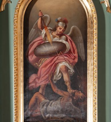 Zdjęcie nr 1: Obraz w kształcie stojącego prostokąta, zamkniętego łukiem półkolistym. W centrum kompozycji znajduje się św. Michał Archanioł w dynamicznej pozie, strącający szatana do piekła. Archanioł ukazany w postawie stojącej, z prawą nogą cofniętą do tyłu, lewą depczący szatana, z podniesioną prawą ręką do góry, w której trzyma płomienisty miecz skierowany ostrzem w dół, a w lewej owalną tarczę z napisem „KTÓŻ JAK BÓG?”. Od miecza biegnie zygzakiem piorun w stronę szatana. Twarz archanioła trójkątna, z długim i prostym nosem, wzrokiem skierowanym w dół. Włosy średniej długości, kręcone, rozwiane do tyłu. Archanioł ubrany jest w zbroję legionisty rzymskiego: ma białą tunikę obszytą złotą lamówką na brzegu, srebrny pancerz, hełm z trójkolorowym pióropuszem, rzymskie sandały oraz czerwony płaszcz rozwiany na wietrze; natomiast na plecach ma białe skrzydła. Na dole kompozycji ukazany jest szatan w pozycji leżącej z głową z prawej strony obrazu, lewą rękę wznoszący ku górze. Twarz owalna z rogami na czole, karnacja ciemna. Ubrany jest w białą szatę, odsłaniającą nagie ramiona i nogi; na plecach ma szare skrzydła nietoperza. Tło jednolite, szare, rozjaśnione w górnej części obrazu. Rama drewniana, złocona, od wewnątrz profilowana, od zewnątrz zdobiona astragalem.
