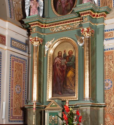 Zdjęcie nr 2: Ołtarz architektoniczny, jednoosiowy, jednokondygnacyjny ze zwieńczeniem. Mensa ołtarzowa prostopadłościenna, antepedium ujęte w ramę z dekoracją ornamentalną z greckim krzyżem pośrodku. Tabernakulum w formie prostopadłościennej skrzynki, ujęte po bokach parą kanelowanych pilastrów, wspierających profilowany gzyms i trójkątny przyczółek, za którym stoi prosty tron wystawienia w formie podwyższonego cokołu. Drzwiczki w kształcie stojącego prostokąta z wpisaną w polu złoconą dekoracją winnej latorośli i motywem kielicha z hostią. Retabulum ołtarzowe wsparte na dwustrefowym cokole, ujęte po bokach parą zdwojonych pilastrów. Kondygnacja flankowana parą złoconych kolumn z kompozytowymi kapitelami, ustawionych na tle pilastrów. Podpory wspierają pełne belkowanie wyłamane nad polem środkowym. Na osi kolumn usadzona jest para klęczących aniołów. W polu głównym obraz w kształcie stojącego prostokąta zakończonego łukiem półkolistym przedstawiający świętych apostołów: Filipa i Jakuba. W górnych przyłuczach pola środkowego para gałązek palmowych przeplecionych przez wianki. Fryz zdobiony wicią z liści akantu, na impostach rozetki, wyżej czerwony gzyms dekorowany kostkowaniem i kimationem. Zwieńczenie w kształcie stojącego prostokąta, flankowane parą kanelowanych pilastrów o korynckich kapitelach podtrzymujących wyłamany gzyms w kształcie łuku nadwieszonego. W polu owalny obraz św. Mikołaja. U szczytu zatknięta promienista gloria z wpisanym pośrodku monogramem IHS na czerwonym tle w wieńcu utworzonym z obłoków. Struktura polichromowana w kolorze jasnozielonym, detale, ornamentyka i profilowania złocone i srebrzone.