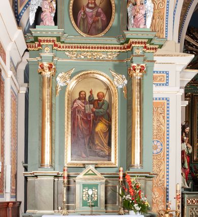 Zdjęcie nr 3: Ołtarz architektoniczny, jednoosiowy, jednokondygnacyjny ze zwieńczeniem. Mensa ołtarzowa prostopadłościenna, antepedium ujęte w ramę z dekoracją ornamentalną z greckim krzyżem pośrodku. Tabernakulum w formie prostopadłościennej skrzynki, ujęte po bokach parą kanelowanych pilastrów, wspierających profilowany gzyms i trójkątny przyczółek, za którym stoi prosty tron wystawienia w formie podwyższonego cokołu. Drzwiczki w kształcie stojącego prostokąta z wpisaną w polu złoconą dekoracją winnej latorośli i motywem kielicha z hostią. Retabulum ołtarzowe wsparte na dwustrefowym cokole, ujęte po bokach parą zdwojonych pilastrów. Kondygnacja flankowana parą złoconych kolumn z kompozytowymi kapitelami, ustawionych na tle pilastrów. Podpory wspierają pełne belkowanie wyłamane nad polem środkowym. Na osi kolumn usadzona jest para klęczących aniołów. W polu głównym obraz w kształcie stojącego prostokąta zakończonego łukiem półkolistym przedstawiający świętych apostołów: Filipa i Jakuba. W górnych przyłuczach pola środkowego para gałązek palmowych przeplecionych przez wianki. Fryz zdobiony wicią z liści akantu, na impostach rozetki, wyżej czerwony gzyms dekorowany kostkowaniem i kimationem. Zwieńczenie w kształcie stojącego prostokąta, flankowane parą kanelowanych pilastrów o korynckich kapitelach podtrzymujących wyłamany gzyms w kształcie łuku nadwieszonego. W polu owalny obraz św. Mikołaja. U szczytu zatknięta promienista gloria z wpisanym pośrodku monogramem IHS na czerwonym tle w wieńcu utworzonym z obłoków. Struktura polichromowana w kolorze jasnozielonym, detale, ornamentyka i profilowania złocone i srebrzone.