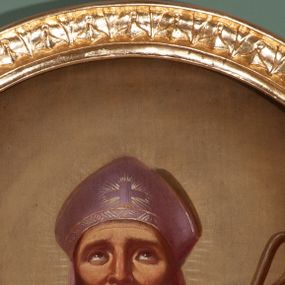 Zdjęcie nr 1: Obraz w kształcie owalu z przedstawieniem św. Mikołaja. Święty ukazany w półpostaci, frontalnie, z prawą ręką wzniesioną w geście błogosławieństwa, z pastorałem w lewej, w której przytrzymuje również księgę. Twarz szeroka o wyraźnie podkreślonych kościach policzkowych, oczy wzniesione ku górze, broda siwa i gęsta. Ubrany jest w białą albę, różowy i szeroki ornat z zieloną podszewką oraz biały paliusz. Na głowie ma założoną fioletową infułę, zdobioną prostym krzyżykiem. Pastorał o prostych formach z zawiniętą krzywaśnią, bez zdobień. Księga w czerwonej oprawie z napisem „S(więty) Jan / Chryzostom / [...]”. Tło jednolite, ciemnobrązowe, rozjaśnione wokół głowy świętego. Rama drewniana, złocona, dekorowana kimationem.

