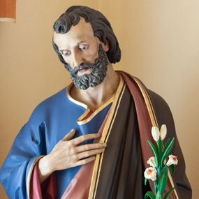 Zdjęcie nr 1: Rzeźba ustawiona na niskim, prostopadłościennym cokole o ściętych narożach, pomalowanym na kolor zielony. Święty Józef został ukazany w całej postaci, w postawie stojącej, w delikatnym kontrapoście, z lewą nogą ugiętą w kolanie, z prawą ręką złożoną na piersi, z gałązką białej lilii w lewej dłoni widocznej na wysokości biodra. Święty Józef ubrany jest w niebieską, długą suknię z czerwoną podszewką, z długimi rękawami oraz w brązowy płaszcz z różową podszewką. Szaty na brzegach złocone. Twarz szeroka, z długim i wąskim nosem, wzrokiem skierowanym w dół, okolona kędzierzawą, krótką brodą oraz średniej długości, ciemnymi włosami. Na dłoniach zaznaczone żyłkowanie. Polichromia w odsłoniętych partiach ciała naturalistyczna. 

