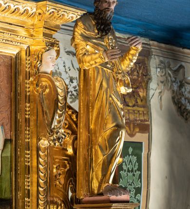 Zdjęcie nr 16: Ołtarz przyścienny, dwukondygnacyjny, jednoosiowy o formach architektonicznych; uszaty. Mensa drewniana, prostopadłościenna; antependium ujęte płaskorzeźbioną, złoconą ramą z dekoracją akantową. Lico malowane z monogramem maryjnym w otoczeniu barwnej dekoracji roślinno-kwiatowej na jasnobeżowym tle. W predelli rama w kształcie leżącego prostokąta ujęta ornamentem kartuszowym mieszcząca pierwotnie niezachowaną dekorację malarską. Nastawa ustawiona na wysokim cokole, ujęta kompozytowymi kolumnami dźwigającymi przełamujące się na osiach podpór pełne belkowanie z kostkowanym achitrawem, płaskorzeźbionym w motyw akantu i uskrzydlonych główek anielskich fryzem oraz wydatnym gzymsem. Kolumny w jednej trzeciej wysokości ujęte profilowanymi opaskami; trzony poniżej opasek zdobione motywem główek anielskich; powyżej płaskorzeźbiona dekoracja arabeskowa. W polu ołtarza prostokątna rama zamknięta łukiem półokrągłym mieszcząca obraz św. Mikołaja; w przyłuczach ramy umieszczone płaskorzeźbione, uskrzydlone główki anielskie. Kondygnacja druga ujęta hermowymi pilastrami dźwigającymi uproszczone belkowanie z wydatnym gzymsem. W polu obraz św. Benedykta o kształcie stojącego prostokąta w złoconej, profilowanej ramie. Na osiach kolumn, ustawione rzeźby św. Piotra (z prawej) i św. Pawła (z lewej) na tle esowatych wolut. Całość nastawy ujęta ażurowymi uszami utworzonymi z ornamentu okuciowego mieszczącymi nisze z rzeźbami św. Cecylii (z lewej) oraz św. Teresy z Avila (z prawej) umieszczonymi na tle muszli. Ponad niszami maszkarony trzymające w pyskach spływające do dołu draperie. Struktura ołtarza oraz partie szat postaci złocone; karnacje rzeźb polichromowane.
