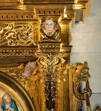 Zdjęcie nr 15: Ołtarz przyścienny, dwukondygnacyjny, jednoosiowy o formach architektonicznych; uszaty. Mensa drewniana, prostopadłościenna; antependium ujęte płaskorzeźbioną, złoconą ramą z dekoracją akantową. Lico malowane z monogramem maryjnym w otoczeniu barwnej dekoracji roślinno-kwiatowej na jasnobeżowym tle. W predelli rama w kształcie leżącego prostokąta ujęta ornamentem kartuszowym mieszcząca pierwotnie niezachowaną dekorację malarską. Nastawa ustawiona na wysokim cokole, ujęta kompozytowymi kolumnami dźwigającymi przełamujące się na osiach podpór pełne belkowanie z kostkowanym achitrawem, płaskorzeźbionym w motyw akantu i uskrzydlonych główek anielskich fryzem oraz wydatnym gzymsem. Kolumny w jednej trzeciej wysokości ujęte profilowanymi opaskami; trzony poniżej opasek zdobione motywem główek anielskich; powyżej płaskorzeźbiona dekoracja arabeskowa. W polu ołtarza prostokątna rama zamknięta łukiem półokrągłym mieszcząca obraz św. Mikołaja; w przyłuczach ramy umieszczone płaskorzeźbione, uskrzydlone główki anielskie. Kondygnacja druga ujęta hermowymi pilastrami dźwigającymi uproszczone belkowanie z wydatnym gzymsem. W polu obraz św. Benedykta o kształcie stojącego prostokąta w złoconej, profilowanej ramie. Na osiach kolumn, ustawione rzeźby św. Piotra (z prawej) i św. Pawła (z lewej) na tle esowatych wolut. Całość nastawy ujęta ażurowymi uszami utworzonymi z ornamentu okuciowego mieszczącymi nisze z rzeźbami św. Cecylii (z lewej) oraz św. Teresy z Avila (z prawej) umieszczonymi na tle muszli. Ponad niszami maszkarony trzymające w pyskach spływające do dołu draperie. Struktura ołtarza oraz partie szat postaci złocone; karnacje rzeźb polichromowane.
