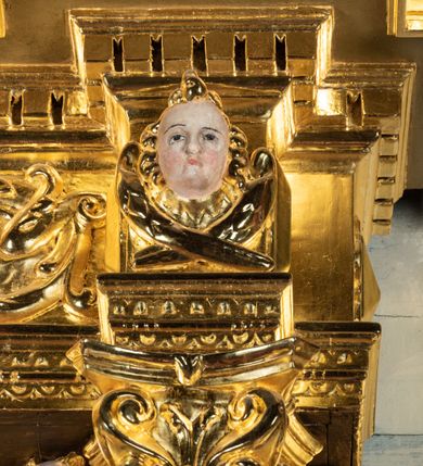 Zdjęcie nr 25: Ołtarz przyścienny, dwukondygnacyjny, jednoosiowy o formach architektonicznych; uszaty. Mensa drewniana, prostopadłościenna; antependium ujęte płaskorzeźbioną, złoconą ramą z dekoracją akantową. Lico malowane z monogramem maryjnym w otoczeniu barwnej dekoracji roślinno-kwiatowej na jasnobeżowym tle. W predelli rama w kształcie leżącego prostokąta ujęta ornamentem kartuszowym mieszcząca pierwotnie niezachowaną dekorację malarską. Nastawa ustawiona na wysokim cokole, ujęta kompozytowymi kolumnami dźwigającymi przełamujące się na osiach podpór pełne belkowanie z kostkowanym achitrawem, płaskorzeźbionym w motyw akantu i uskrzydlonych główek anielskich fryzem oraz wydatnym gzymsem. Kolumny w jednej trzeciej wysokości ujęte profilowanymi opaskami; trzony poniżej opasek zdobione motywem główek anielskich; powyżej płaskorzeźbiona dekoracja arabeskowa. W polu ołtarza prostokątna rama zamknięta łukiem półokrągłym mieszcząca obraz św. Mikołaja; w przyłuczach ramy umieszczone płaskorzeźbione, uskrzydlone główki anielskie. Kondygnacja druga ujęta hermowymi pilastrami dźwigającymi uproszczone belkowanie z wydatnym gzymsem. W polu obraz św. Benedykta o kształcie stojącego prostokąta w złoconej, profilowanej ramie. Na osiach kolumn, ustawione rzeźby św. Piotra (z prawej) i św. Pawła (z lewej) na tle esowatych wolut. Całość nastawy ujęta ażurowymi uszami utworzonymi z ornamentu okuciowego mieszczącymi nisze z rzeźbami św. Cecylii (z lewej) oraz św. Teresy z Avila (z prawej) umieszczonymi na tle muszli. Ponad niszami maszkarony trzymające w pyskach spływające do dołu draperie. Struktura ołtarza oraz partie szat postaci złocone; karnacje rzeźb polichromowane.
