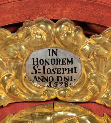 Zdjęcie nr 10: Ołtarz przyścienny o formach architektonicznych, jednoosiowy, jednokondygnacyjny ze zwieńczeniem; ujęty akantowymi uszami. Mensa prostopadłościenna; antepedium malowane w symetryczne motywy roślinno-kwiatowe na jasnobeżowym tle; ujęte złoconą ramą w kształcie leżącego prostokąta o wypukłych krótszych bokach. Nastawa ujęta parą kolumn umieszczonych na wysokich, prostopadłościennych postumentach. Trzony kolumn skręcone, oplecione kwiatowymi girlandami; kapitele kompozytowe, złocone. W polu ołtarza złocona, profilowana rama w kształcie stojącego prostokąta, mieszcząca obraz z przedstawieniem św. Józefa. Kolumny dźwigają pełne belkowanie przełamane na osiach podpór oraz odcinki trójkątnego przyczółka, na których pełnoplastyczne figurki aniołów. W partii fryzu złocony ornament akantowy oraz rozetki. Zwieńczenie w kształcie równoramiennego trapezu o wklęsłych bokach, zamknięte od góry gzymsem wklęsło-wypukłym. W polu owalna, złocona rama w formie wieńca laurowego mieszcząca obraz przedstawiający św. Jana Ewangelistę, ponad którym owalny, akantowy kartusz z napisem „IN / HONOREM S(ANCTI) JOSEPHI / ANNO DOMINI 1528”. Nastawa ujęta ażurowymi, złoconymi i srebrzonymi uszami utworzonymi z suchego akantu. Struktura ołtarza marmoryzowana w odcieniach czerwieni; dekoracja snycerska srebrzona i złocona, trzony kolumn czarne.

