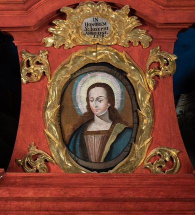 Zdjęcie nr 7: Ołtarz przyścienny o formach architektonicznych, jednoosiowy, jednokondygnacyjny ze zwieńczeniem; ujęty akantowymi uszami. Mensa prostopadłościenna; antepedium malowane w symetryczne motywy roślinno-kwiatowe na jasnobeżowym tle; ujęte złoconą ramą w kształcie leżącego prostokąta o wypukłych krótszych bokach. Nastawa ujęta parą kolumn umieszczonych na wysokich, prostopadłościennych postumentach. Trzony kolumn skręcone, oplecione kwiatowymi girlandami; kapitele kompozytowe, złocone. W polu ołtarza złocona, profilowana rama w kształcie stojącego prostokąta, mieszcząca obraz z przedstawieniem św. Józefa. Kolumny dźwigają pełne belkowanie przełamane na osiach podpór oraz odcinki trójkątnego przyczółka, na których pełnoplastyczne figurki aniołów. W partii fryzu złocony ornament akantowy oraz rozetki. Zwieńczenie w kształcie równoramiennego trapezu o wklęsłych bokach, zamknięte od góry gzymsem wklęsło-wypukłym. W polu owalna, złocona rama w formie wieńca laurowego mieszcząca obraz przedstawiający św. Jana Ewangelistę, ponad którym owalny, akantowy kartusz z napisem „IN / HONOREM S(ANCTI) JOSEPHI / ANNO DOMINI 1528”. Nastawa ujęta ażurowymi, złoconymi i srebrzonymi uszami utworzonymi z suchego akantu. Struktura ołtarza marmoryzowana w odcieniach czerwieni; dekoracja snycerska srebrzona i złocona, trzony kolumn czarne.
