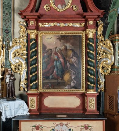 Zdjęcie nr 1: Ołtarz przyścienny o formach architektonicznych; jednoosiowy, jednokondygnacyjny ze zwieńczeniem, uszaty. Mensa prostopadłościenna; antepedium malowane z trzema kwiatowymi medalionami mieszczącymi literę J, monogram maryjny oraz literę A na jasnobeżowym tle. Poniżej środkowego medalionu płonące serce przebite krzyżem i kotwicą. W predelli nisza w kształcie poziomego prostokąta z wypukłymi krótszymi bokami, zapewne pierwotnie mieszcząca niezachowany obraz. Nastawa ujęta parą kolumn umieszczonych na wysokich, prostopadłościennych postumentach. Trzony kolumn skręcone, oplecione kwiatowymi girlandami; kompozytowe kapitele złocone. W polu ołtarza złocona, profilowana rama w kształcie pionowego prostokąta mieszcząca obraz z przedstawieniem św. Anny, św. Joachima i Marii. Kolumny dźwigają pełne belkowanie przełamane na osiach podpór oraz odcinki zbudowanego z wolut przyczółka, na których umieszczono pełnoplastyczne figurki aniołów. W partii fryzu złocony ornament akantowy przepleciony srebrzoną wstęgą  oraz rozetki. Zwieńczenie w kształcie trapezu równoramiennego o wklęsłych bokach, zamknięte od góry gzymsem w formie łuku nadwieszonego. W polu owalna, złocona rama w kształcie wieńca laurowego mieszcząca obraz przedstawiający św. Sebastiana, ponad którym akantowy kartusz owalny z inskrypcją „IN HONOREM S(ANCTI) JOACHIM ANNO DOMINI 1518”. Nastawa ujęta ażurowymi, złoconymi i srebrzonymi uszami utworzonymi z suchego akantu oraz karbowanej wstęgi. Struktura ołtarza „marmoryzowana” w odcieniach czerwieni; dekoracja snycerska srebrzona i złocona, trzony kolumn czarne.



