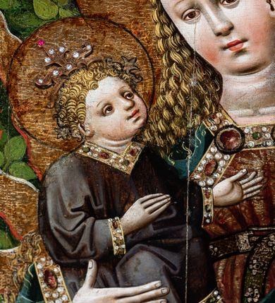 Zdjęcie nr 13: Obraz w kształcie stojącego prostokąta, w złoconej i profilowanej ramie. W centrum kompozycji ukazana Matka Boska z Dzieciątkiem stojąca na półksiężycu, na tle krajobrazu. Maria ukazana całopostaciowo, frontalnie, z głową pochyloną nieznacznie w lewo — w kierunku Jezusa, którego trzyma na swoim prawym przedramieniu. Postać przedstawiona jako młoda, jasnowłosa kobieta, o jasnej karnacji z delikatnie zaznaczonym rumieńcem. Owalną twarz o wysokim czole, miękko zarysowanym podbródku oraz drobnych, pełnych ustach okalają długie, falujące włosy, które opadają na ramiona i plecy postaci. Oczy o migdałowatym kształcie wpatrzone przed siebie. Na głowie Marii widoczna złota korona typu otwartego zdobiona perłami oraz kamieniami szlachetnymi; wokół głowy złocony nimb. Postać ubrana w czerwoną suknię w złote wzory, spiętą w talii brązowym paskiem tłoczonym we wzór kratki, zapinanym metalową sprzączką. Otwory w pasku nabijane metalowymi nitami w kształcie pięciolistnych kwiatów. Dolna krawędź sukni obramiona szeroką lamówką wyszywaną perłami oraz kamieniami szlachetnymi. Na ramionach Marii obszerny, bogato zdobiony płaszcz wykonany z ciężkiej, granatowej tkaniny dekorowanej motywem owoców granatu oraz liści dębu. Jego brzegi lamowane szeroką, złotą bordiurą zdobioną umieszczonymi na przemian szmaragdowymi i rubinowymi kaboszonami oraz perłami; pod szyją ozdobna zapinka. Spod płaszcza miejscami widoczna purpurowa podszewka. Na wysokości bioder postaci okrycie tworzy obfite fałdy, które Maria podtrzymuje swoją prawą dłonią. Na lewym przedramieniu Matki Boskiej siedzące Dzieciątko Jezus ukazane w ujęciu w trzech czwartych, zwrócone w kierunku Marii, do której wznosi obie dłonie i głowę. Twarz Dzieciątka okrągła, usta i nos drobne. Jezus spogląda na Marię. Jego jasnowłosą głowę, na której ukazana złota korona zdobiona perłami oraz kamieniami szlachetnymi otacza złoty nimb. Dzieciątko ubrane jest w ciemnobrązową tunikę lamowaną dołem, pod szyją i wokół rękawów szeroką taśmą wyszywaną kamieniami szlachetnymi. Obie postaci otacza gloria utworzona ze złotych promieni, pomiędzy którymi widoczne ciemnopomarańczowe języki ognia. U stóp Marii ukazana kwietna łąka z realistycznie przedstawioną roślinnością: paprociami, krzewami poziomek i jagód oraz kwiatami, wśród których można rozpoznać ciemnofioletowe orliki i fiołki. Powyżej, na dalszym planie gęstwina drzew o cienkich, brązowych pniach oraz jasnozielonych liściach, tworzących zwartą strukturę układającą się w kształt łuku ostrego. W górnych narożach obrazu, ponad linią drzew dwie postaci jasnowłosych aniołów w długich, ciemnogranatowych tunikach. Anioł z lewej trzyma banderolę z napisem: „Regina celi letare all[elui]a”, anioł z prawej z napisem: „quia quem meristi por[tare]”. Rozpostarte skrzydła aniołów ukazane w kolorach zielonym, ciemnogranatowym oraz purpurowym.
