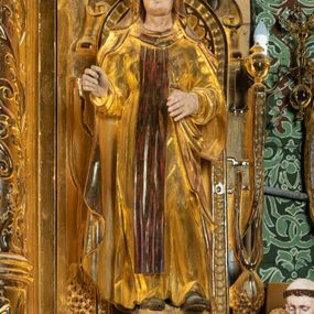 Zdjęcie nr 1: Rzeźba drążona, ustawiona na niewielkim prostopadłościennej podstawie na tle niszy w prawym naddatku ołtarza. Przedstawia św. Teresę z Avila ukazaną frontalnie, w pozycji stojącej, w lekkim kontrapoście z lewą nogą ugiętą w kolanie i wysunięta do przodu. Święta została przedstawiona jako dojrzała kobieta o owalnej twarzy z pełnymi policzkami, wyraźnie zaznaczonym niewielkim podbródkiem, wydatnym prostym nosem oraz migdałowatymi, wpatrzonymi na wprost oczami. Włosy niewidoczne, zakryte welonem zakonnym. Prawa ręka postaci ugięta w łokciu i wysunięta do przodu. Układ palców prawej dłoni wskazuje, że być może w tym miejscu postać trzymała atrybut, który nie zachował się do dziś. Lewa ręka również ugięta w łokciu i swobodnie wysunięta przed siebie. Święta jest ubrana w obszerny złoty habit przepasany na wysokości talii, na którym widoczny szkaplerz oraz płaszcz. Z lewej strony poła płaszcza swobodnie opada w dół, z prawej tkanina tworzy łyżkowatą fałdę umocowaną przy pasku habitu. Spod habitu widoczne czubki brązowych butów o zaokrąglonych noskach. Partie karnacji polichromowane, szaty w całości złocone.
