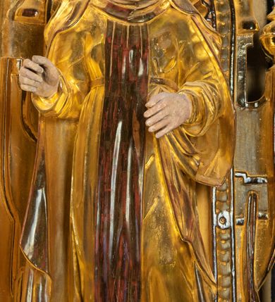 Zdjęcie nr 4: Rzeźba drążona, ustawiona na niewielkim prostopadłościennej podstawie na tle niszy w prawym naddatku ołtarza. Przedstawia św. Teresę z Avila ukazaną frontalnie, w pozycji stojącej, w lekkim kontrapoście z lewą nogą ugiętą w kolanie i wysunięta do przodu. Święta została przedstawiona jako dojrzała kobieta o owalnej twarzy z pełnymi policzkami, wyraźnie zaznaczonym niewielkim podbródkiem, wydatnym prostym nosem oraz migdałowatymi, wpatrzonymi na wprost oczami. Włosy niewidoczne, zakryte welonem zakonnym. Prawa ręka postaci ugięta w łokciu i wysunięta do przodu. Układ palców prawej dłoni wskazuje, że być może w tym miejscu postać trzymała atrybut, który nie zachował się do dziś. Lewa ręka również ugięta w łokciu i swobodnie wysunięta przed siebie. Święta jest ubrana w obszerny złoty habit przepasany na wysokości talii, na którym widoczny szkaplerz oraz płaszcz. Z lewej strony poła płaszcza swobodnie opada w dół, z prawej tkanina tworzy łyżkowatą fałdę umocowaną przy pasku habitu. Spod habitu widoczne czubki brązowych butów o zaokrąglonych noskach. Partie karnacji polichromowane, szaty w całości złocone.
