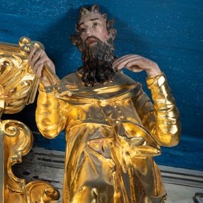 Zdjęcie nr 1: Rzeźba pełnoplastyczna ustawiona na niewielkim prostopadłościennym postumencie zwieńczonym złoconym gzymsem. Święty Piotr ukazany frontalnie w pozycji stojącej, w lekkim kontrapoście z prawą noga lekko ugiętą w kolanie i wysuniętą do przodu. Głowa zwrócona w trzech czwartych w lewo w kierunku osi ołtarza. Postać przedstawiona jako dojrzały mężczyzna o szczupłej, pociągłej twarzy okolonej ciemnym zarostem – wąsami i długą kędzierzawą brodą; włosy krótkie, ciemne i kręcone. Ręce zgięte w łokciach, przedramiona podniesione do góry. W prawej dłoni święty trzyma dwa klucze, lewa dłoń luźno opadająca, skierowana w lewo. Święty jest ubrany w długą, obficie fałdowaną, przewiązaną w pasie złotą szatę z długimi rękawami. Spod szaty wystają bose stopy. Partie karnacji polichromowane, szaty i atrybut złocone.