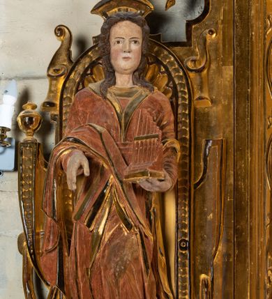 Zdjęcie nr 1: Rzeźba drążona, umieszczona w ołtarzu św. Mikołaja, na tle niszy lewego naddatku ołtarza. Święta Cecylia przedstawiona frontalnie w pozycji stojącej, w lekkim kontrapoście z lewą nogą lekko ugiętą i wysuniętą do przodu. Ukazana jako młoda, długowłosa kobieta o owalnej twarzy z pełnymi policzkami i niewielkim, wyraźnie zaznaczonym podbródkiem. Oczy o migdałowatym kształcie wpatrzone przed siebie, niewielkie usta zaznaczone czerwienią; mocno zaakcentowany, prosty nos. Głowę okalają długie, lekko falowane włosy opadające symetrycznie na ramiona postaci. Święta w lewej ręce trzyma złocony portatyw; prawa ręka zgięta w łokci i wysunięta nieco do przodu. Postać ubrana jest w długą, złotą suknię oraz szatę wierzchnią z długimi rękawami oraz trójkątnie wyciętym dekoltem wykończonym kołnierzem. Przez prawe przedramię postaci przewieszony fałd sukni. Spod sukni widoczne brązowe pantofle o miękko zakończonych noskach. Partie karnacji oraz włosów polichromowane, szaty i portatyw złocone.