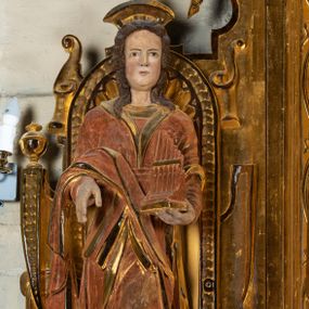 Zdjęcie nr 1: Rzeźba drążona, umieszczona w ołtarzu św. Mikołaja, na tle niszy lewego naddatku ołtarza. Święta Cecylia przedstawiona frontalnie w pozycji stojącej, w lekkim kontrapoście z lewą nogą lekko ugiętą i wysuniętą do przodu. Ukazana jako młoda, długowłosa kobieta o owalnej twarzy z pełnymi policzkami i niewielkim, wyraźnie zaznaczonym podbródkiem. Oczy o migdałowatym kształcie wpatrzone przed siebie, niewielkie usta zaznaczone czerwienią; mocno zaakcentowany, prosty nos. Głowę okalają długie, lekko falowane włosy opadające symetrycznie na ramiona postaci. Święta w lewej ręce trzyma złocony portatyw; prawa ręka zgięta w łokci i wysunięta nieco do przodu. Postać ubrana jest w długą, złotą suknię oraz szatę wierzchnią z długimi rękawami oraz trójkątnie wyciętym dekoltem wykończonym kołnierzem. Przez prawe przedramię postaci przewieszony fałd sukni. Spod sukni widoczne brązowe pantofle o miękko zakończonych noskach. Partie karnacji oraz włosów polichromowane, szaty i portatyw złocone.