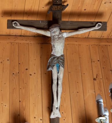 Zdjęcie nr 2: Chrystus ukazany w typie Cristo morte. Ciało przybite do prostego, drewnianego krzyża trzema gwoździami. Chrystus z szeroko rozpostartymi ramionami tworzącymi niemal linię prostą. Głowa przechylona nieznacznie w kierunku prawego barku. Ukazana w cierniowej koronie, spod której sączą się strużki krwi – nieproporcjonalnie duża w stosunku do wychudzonego ciała postaci. Twarz prostokątna z dużymi, zamkniętymi oczami, wydatnym nosem oraz ciemnym zarostem. Włosy długie, spływające na ramiona i plecy postaci w dwóch spiralnie skręconych puklach. Ciało Chrystusa szczupłe o wysmukłych proporcjach, bez wyraźnie zaznaczonej muskulatury. Dłonie, przebite gwoździami zamykają się lekko na wydatnych główkach gwoździ. Po przedramionach spływają cienkie stróżki krwi. Stopy duże, przebite jednym gwoździem. Na prawym boku postaci widoczna krwawiąca rana. Perizonium krótkie, srebrzone, o ostro łamiącej się draperii. Nad głową Chrystusa titulus ze złoconym napisem „INRI” wykonanym gotycką minuskułą.