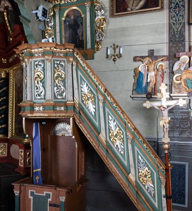 Zdjęcie nr 2: Ambona przyścienna o formach architektonicznych; dostępna jednobiegowymi schodkami od strony prezbiterium. Kosz na rzucie wieloboku, ustawiony na znajdującym się poniżej konfesjonale, ujęty pilastrami o kompozytowych, złoconych kapitelach. Pilastry stojące na wysuniętych przed lico ambony profilowanych postumentach dźwigają wydatny, profilowany i wyłamujący się na osi podpór gzyms. Prostokątne pola kosza są wypełnione złoconym i srebrzonym „suchym” akantem. Fryz i architraw dekorowane złoconym ornamentem kwiatowym. Balustrada schodków pełna o podziałach identycznych jak korpus ambony. Zaplecek ujęty parą pilastrów o kompozytowych, złoconych kapitelach dźwigających pełne, wyłamane na osi podpór belkowanie zwieńczone profilowanym gzymsem. W polu obraz przedstawiający św. Franciszka z Asyżu na tle pejzażu w kształcie stojącego prostokąta zamkniętego łukiem nadwieszonym. Święty został ukazany całopostaciowo, frontalnie w brązowym habicie przepasanym sznurem. W lewej dłoni trzyma zamkniętą księgę oraz lilię, prawą wykonuje gest oratorski. U jego lewego boku przedstawiony jeleń. Całość zaplecka ujęta ażurowymi uszami utworzonymi ze złoconego i srebrzonego „suchego” akantu. Baldachim na rzucie połowy ośmioramiennej gwiazdy, zwieńczony złoconą szyszką ustawioną na ażurowej konsoli utworzonej z akantowych wolut; w podniebiu płaskorzeźbiona gołębica Ducha Świętego na tle glorii promienistej. Struktura malowana na kolor jasnozielony z jasnobrązowymi elementami. Partie ornamentów złocone i srebrzone; trzony pilastrów marmoryzowane w odcieniach pastelowej zieleni. Konfesjonał na rzucie prostokąta. Przedpiersie ujęte parą pilastrów o gładkich, ciemnozielonych trzonach i złoconych, kompozytowych kapitelach. W polu prostokątna, „uszata” płycina malowana na ciemnozielono. Zaplecek gładki z prostokątną płyciną zamkniętą łukiem nadwieszonym mieszczącym złoconą muszlę palmetową. Boki o linii wklęsło-wypukłej zamknięte od góry akantowymi wolutami. Struktura malowana na kolor jasnobrązowy.
