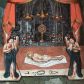 Zdjęcie nr 1: Obraz w kształcie stojącego prostokąta. Na osi kompozycji u dołu ukazane ciało Chrystusa zdjęte z krzyża i ułożone na białym całunie, który rozłożono na czerwonym podium z białym pasem od przodu; ramiona Chrystusa ułożone wzdłuż ciała. Głowa ujęta z prawego profilu, otoczona promienistym nimbem. Oczy zamknięte, włosy i broda siwe. Tors nagi z widoczną raną w boku, wokół bioder owinięte białe perizonium. Na pierwszym planie po bokach, na wyodrębnionych częściach podium ukazane postaci dwóch stojących naprzeciw siebie aniołów trzymających arma Christi. Anioł z lewej strony kompozycji prawą ręką podtrzymuje gąbkę zamieszczoną na długim drzewcu, gest lewej, zbliżonej do policzka, wyraża żal. Anioł z prawej strony obrazu w lewej ręce trzyma włócznię, prawą ręką wykonuje analogiczny gest jak anioł z lewej. Obie postaci przedstawione jako młodzieńcy o długich włosach ubrani w obszerne, granatowe płaszcze. U ich stóp, na białej części podium przedstawione pozostałe narzędzia męki Chrystusa: młotek, gwoździe, korona cierniowa i kleszcze. Na dalszym planie, w głębi kompozycji widoczna półkolista arkada udekorowana czerwoną draperią. Przedstawiono w niej ołtarz, na którym stoją monstrancja promienista z hostią, sześć lichtarzy oraz wazony z kwiatami. Nieco powyżej ukazane trzy podwieszone lampy wieczne w kolorze złotym. W górnych narożnikach, ponad arkadą dekoracyjne motywy zbudowane z trzech ulistnionych gałęzi. Kolorystyka ciemna, chłodna z dominacją szarości i czerni. Obraz oprawiony w ramę z szerokiej, wypukłej listwy zdobionej rodzajem pseudomarmoryzacji w odcieniach brązu.


