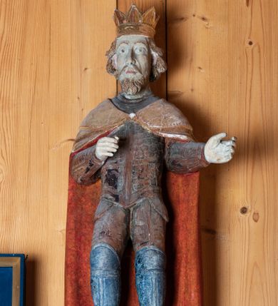 Zdjęcie nr 1: Rzeźba pełnoplastyczna, ścięta z tyłu. Król ukazany w postawie stojącej, frontalnie, z nogami w lekkim rozkroku i ugiętymi w kolanach. Ręce zgięte w łokciach pod kątem prostym z ramionami przylegającymi do tułowia. Przedramiona skierowane w lewo. Głowa wydłużona, jasnobrązowe włosy dłuższe, lekko falowane, odsłaniające uszy, zarost krótki. Wzrok skierowany przed siebie, oczy duże migdałowate, brwi wyraźne, łukowe. Nos długi, wydatny, usta niewielkie. Na głowie postaci złocona korona w typie otwartym. Król ubrany jest w zbroję, na którą składa się krótki, łuskowy pancerz, zarękawia, nabiodrki, nakolanki, nagolennice i trzewiki. Na pancerz narzucony jest długi, złoty płaszcz, podszyty na czerwono, spięty pod szyją okrągłą zapinką. Figura w pełni polichromowana, korona i płaszcz złocone.